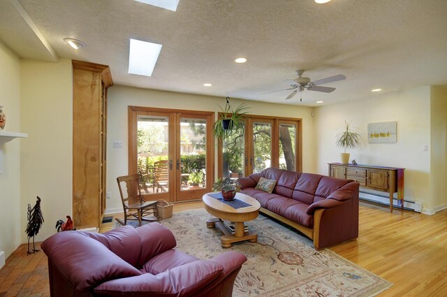 living room with a skylight, french doors, baseboard heating, a textured ceiling, and light wood-type flooring