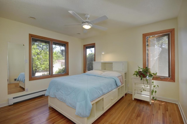 bedroom featuring light wood-style floors, baseboards, baseboard heating, and a ceiling fan