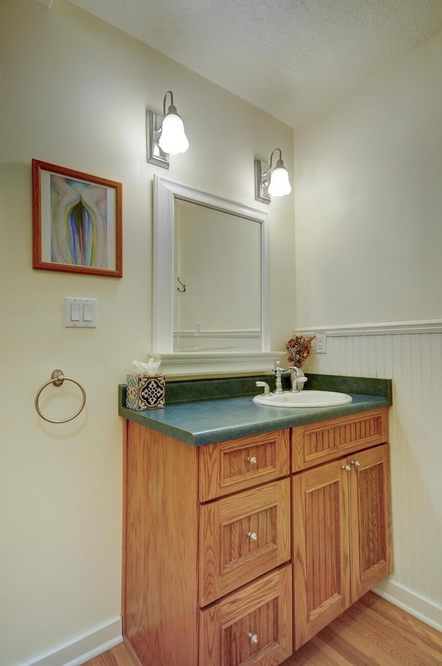 bathroom with baseboards, wainscoting, wood finished floors, a textured ceiling, and vanity