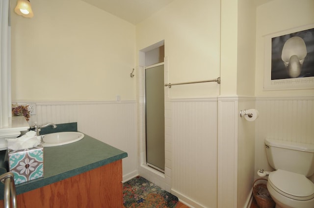 full bathroom featuring a stall shower, wainscoting, vanity, and toilet