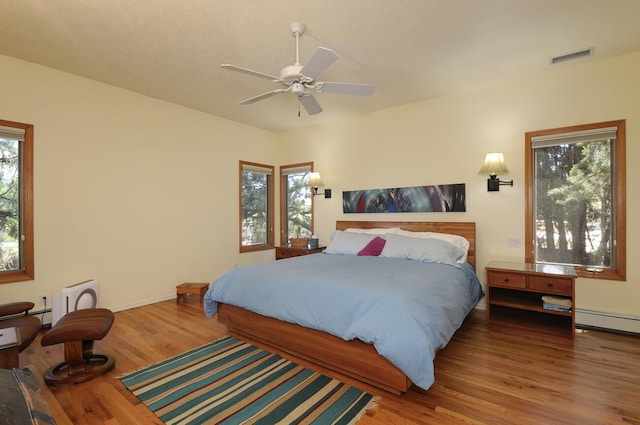 bedroom featuring a ceiling fan, multiple windows, visible vents, and wood finished floors