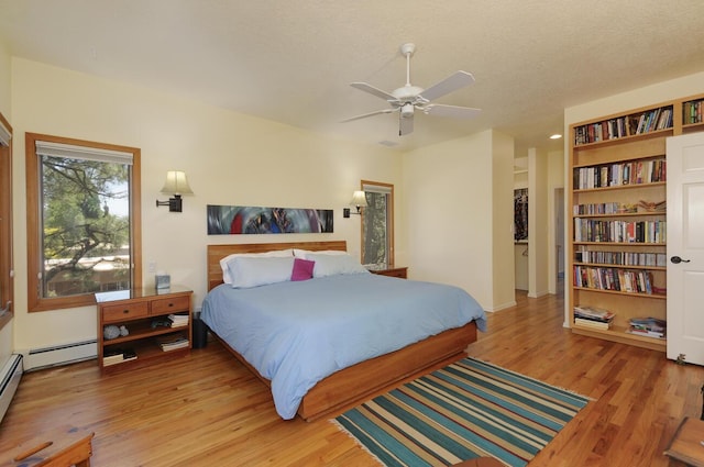 bedroom with a textured ceiling, ceiling fan, baseboard heating, and light wood-type flooring