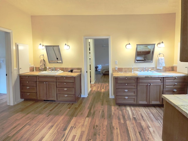 full bath featuring two vanities, a sink, baseboards, and wood finished floors