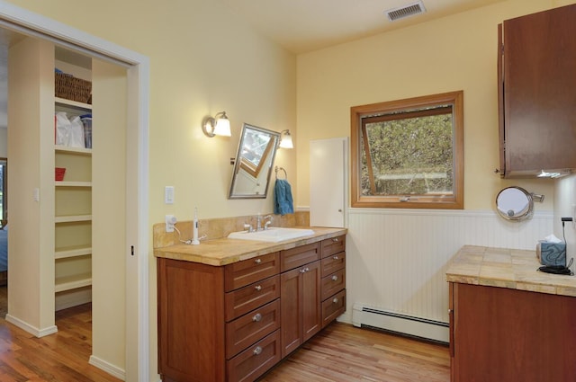 bathroom with a baseboard heating unit, wood finished floors, vanity, visible vents, and a spacious closet