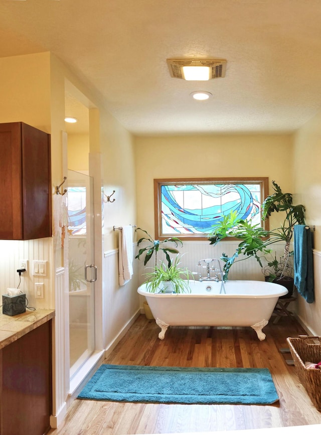 full bathroom with a freestanding tub, a shower stall, visible vents, and wood finished floors