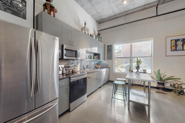 kitchen featuring gray cabinetry, concrete floors, decorative backsplash, appliances with stainless steel finishes, and a sink