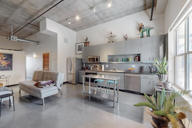 kitchen with concrete floors, open shelves, a high ceiling, a sink, and appliances with stainless steel finishes