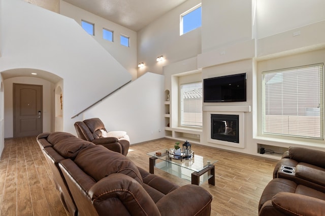 living room featuring arched walkways, a glass covered fireplace, and wood finished floors