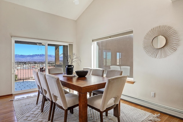 dining area featuring high vaulted ceiling, a baseboard radiator, a mountain view, and hardwood / wood-style flooring