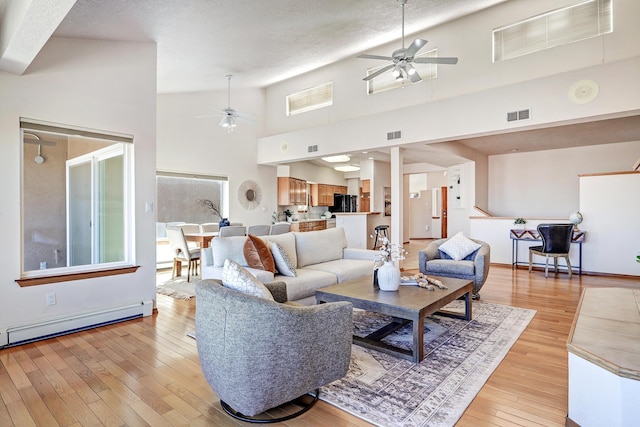 living area featuring a baseboard heating unit, visible vents, light wood-style floors, and ceiling fan