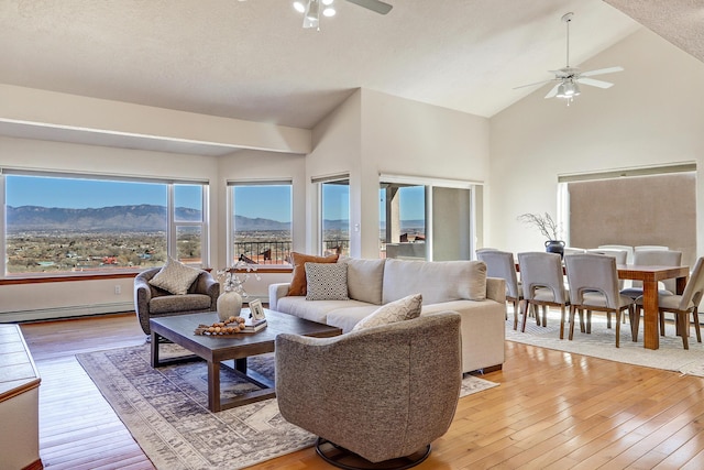 living area with a ceiling fan, baseboard heating, light wood-type flooring, high vaulted ceiling, and a mountain view