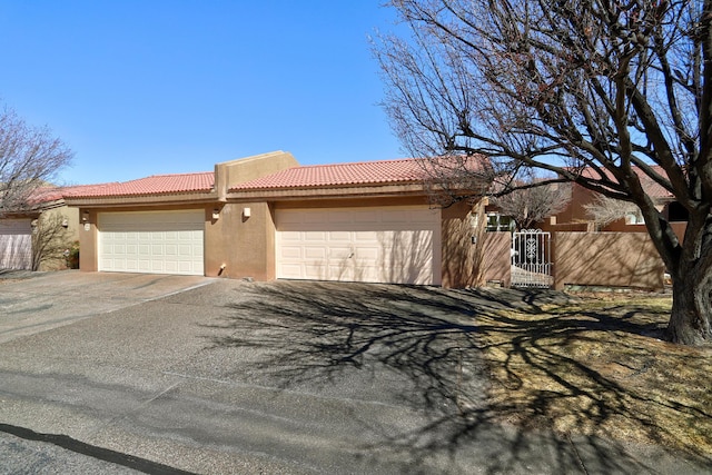 view of front of house with an attached garage, a tile roof, fence, and stucco siding