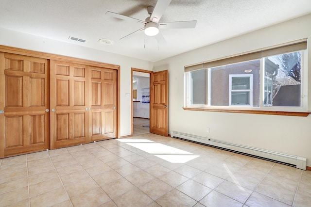 unfurnished bedroom featuring a textured ceiling, light tile patterned flooring, a baseboard heating unit, visible vents, and a closet