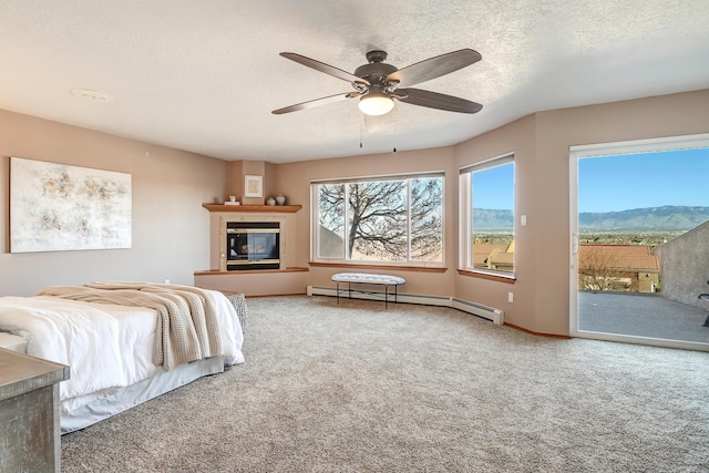 carpeted bedroom with a textured ceiling, a mountain view, a baseboard heating unit, access to outside, and a glass covered fireplace