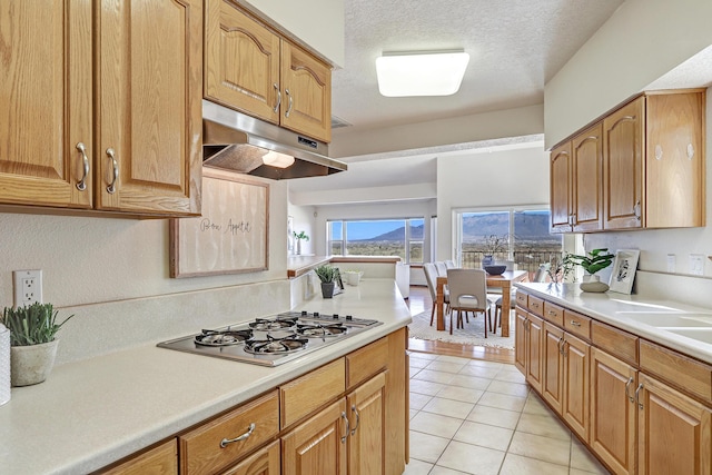 kitchen with light tile patterned floors, light countertops, stainless steel gas stovetop, a textured ceiling, and under cabinet range hood