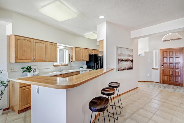 kitchen with light countertops, black refrigerator with ice dispenser, a breakfast bar area, and a sink