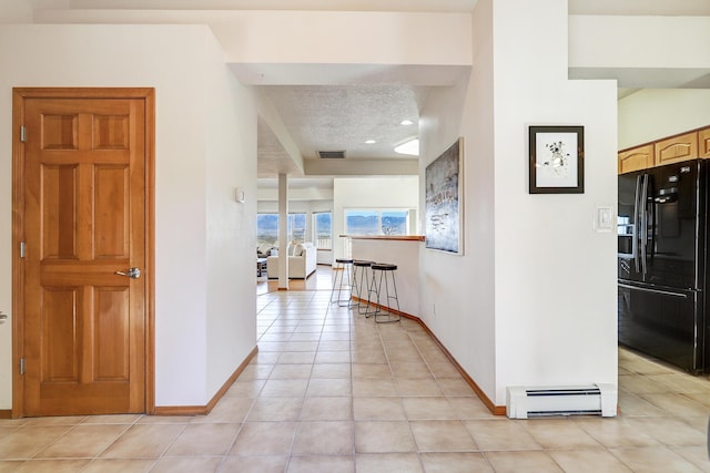 hallway featuring light tile patterned floors, visible vents, baseboards, a textured ceiling, and a baseboard heating unit