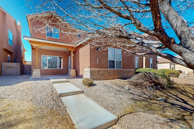 view of front of house featuring stone siding, a tile roof, fence, and stucco siding