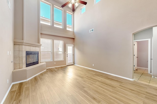 unfurnished living room with arched walkways, visible vents, ceiling fan, light wood-style floors, and a fireplace