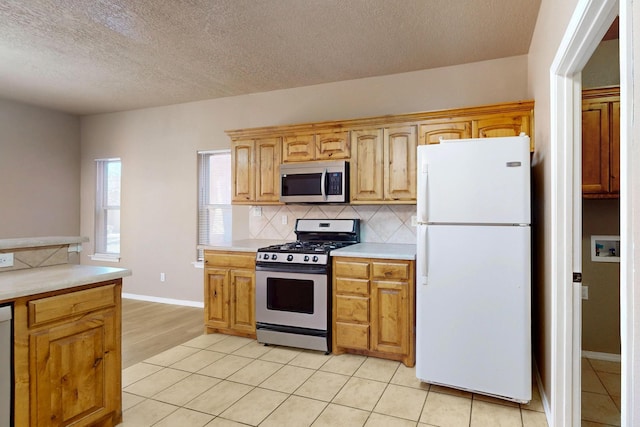 kitchen with a textured ceiling, light tile patterned flooring, stainless steel appliances, light countertops, and tasteful backsplash