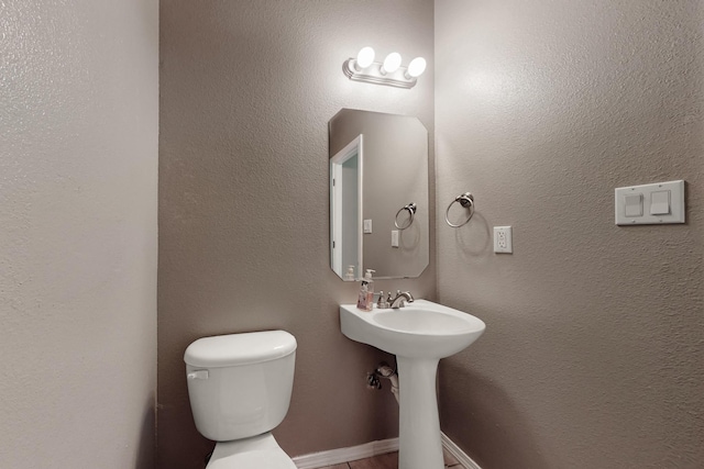 half bath featuring baseboards, a sink, and toilet