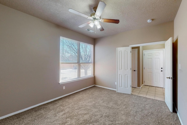 unfurnished bedroom featuring light tile patterned floors, visible vents, light carpet, a textured ceiling, and baseboards