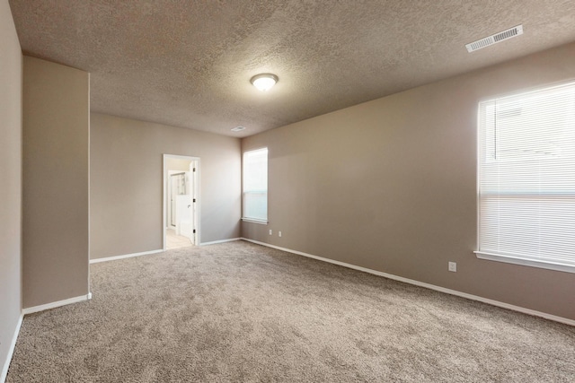 carpeted empty room with a textured ceiling, visible vents, and baseboards