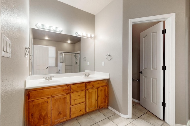 bathroom featuring double vanity, a stall shower, a sink, tile patterned flooring, and baseboards