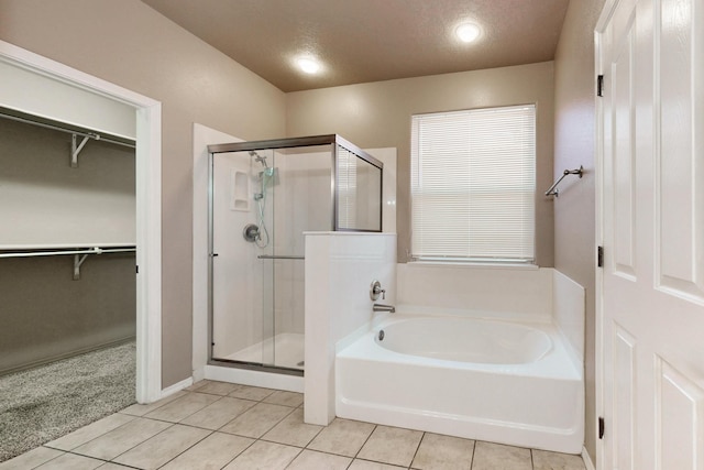 bathroom with a textured ceiling, a shower stall, a bath, tile patterned floors, and a walk in closet