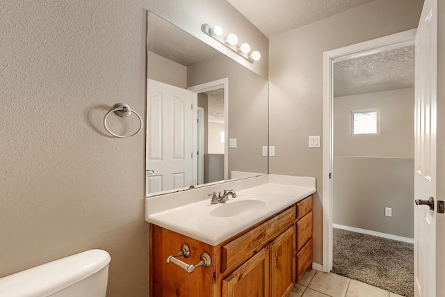 bathroom with toilet, a textured ceiling, vanity, tile patterned flooring, and baseboards