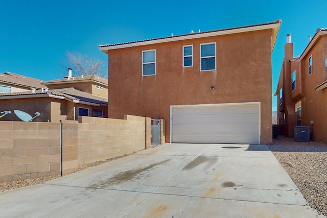 rear view of property with central AC unit, a garage, fence, driveway, and stucco siding