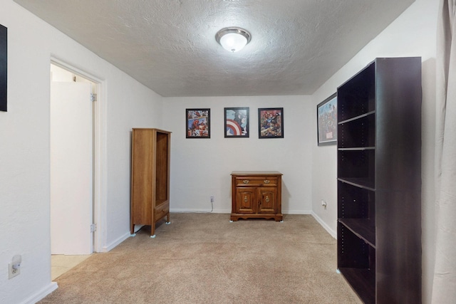 empty room featuring light carpet, a textured ceiling, and baseboards