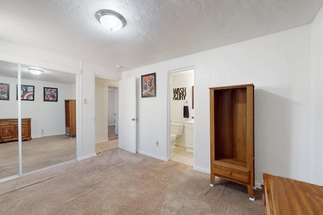 unfurnished bedroom with light colored carpet, connected bathroom, a textured ceiling, and baseboards