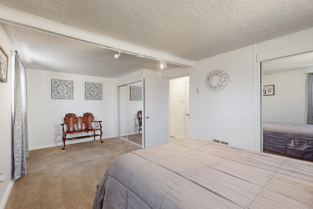 carpeted bedroom with a closet, visible vents, a textured ceiling, and track lighting