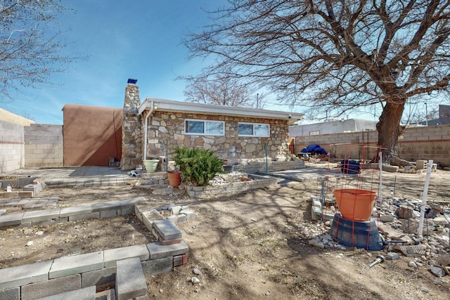 rear view of property featuring stone siding, a fenced backyard, and a chimney