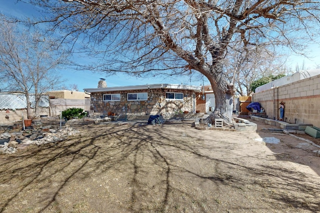 back of property with stone siding, a chimney, and fence