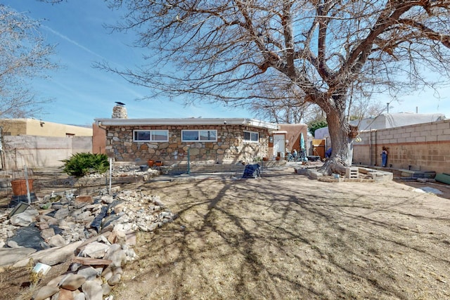 rear view of house with stone siding, a chimney, and fence private yard