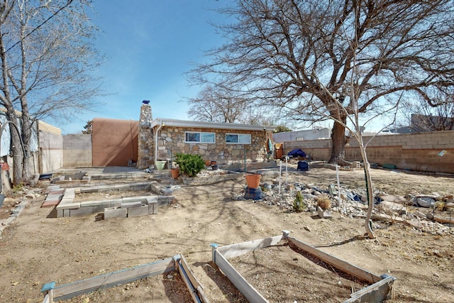 back of house featuring stone siding, a fenced backyard, a vegetable garden, and a chimney