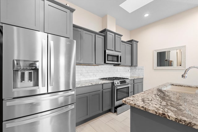 kitchen with tasteful backsplash, appliances with stainless steel finishes, light stone counters, gray cabinets, and a sink