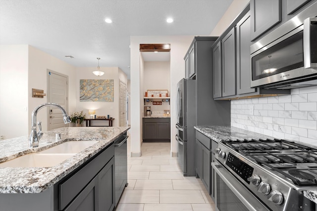 kitchen with stainless steel appliances, light stone counters, backsplash, and a sink