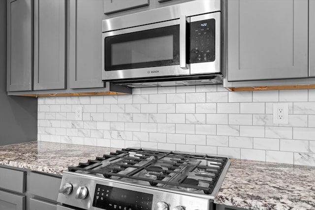 kitchen with tasteful backsplash, gray cabinets, light stone counters, and stainless steel appliances