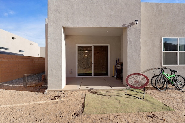 view of exterior entry with a patio, fence, visible vents, and stucco siding