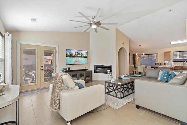 living room with lofted ceiling, arched walkways, ceiling fan with notable chandelier, visible vents, and french doors