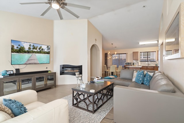 living area with ceiling fan with notable chandelier, arched walkways, and a glass covered fireplace