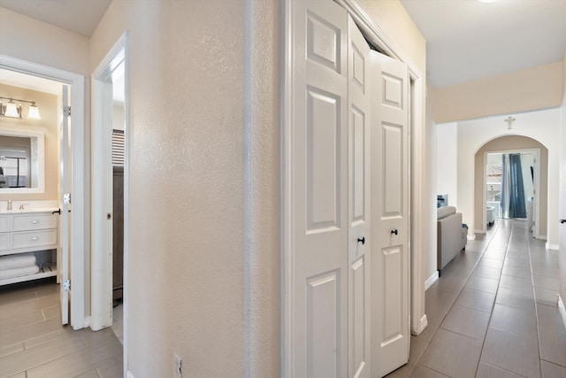 corridor featuring arched walkways, a sink, and baseboards