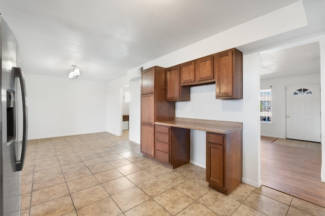 kitchen featuring light tile patterned floors, baseboards, light countertops, stainless steel refrigerator with ice dispenser, and brown cabinetry