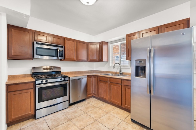 kitchen featuring brown cabinets, light tile patterned floors, stainless steel appliances, light countertops, and a sink