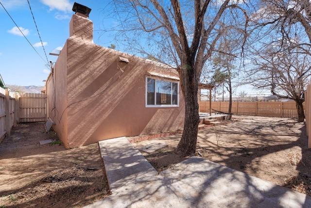 view of side of property featuring a fenced backyard, a chimney, and stucco siding