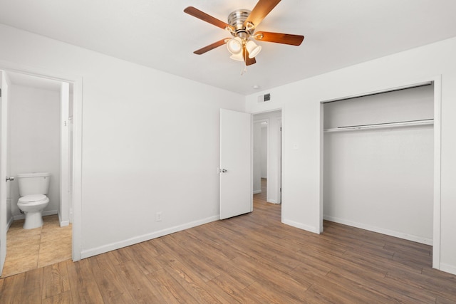 unfurnished bedroom featuring ensuite bath, wood finished floors, a ceiling fan, and baseboards