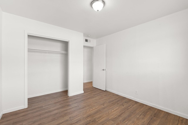 unfurnished bedroom featuring baseboards, a closet, visible vents, and wood finished floors